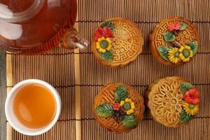 Colorful flower decorated mooncake cut slice half layer Chinese mid autumn festival on bamboo food mat glass teapot white ceramic teacup photo