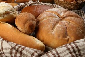 Freshly baked bread loaf bun roll round long mix verity wrapped in checkered kitchen fabric napkin towel wheat flower oil water salt eggs rolling pin slate stone over black background photo