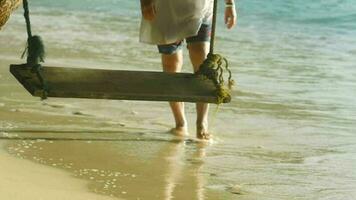 un irreconocible hombre camina a lo largo el costa. olas rodar en el playa. paraíso vacaciones en el isla. columpio en un palma árbol video