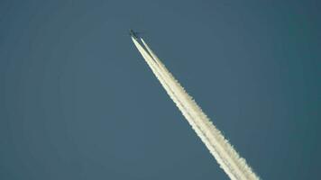 Airplane flies overhead on clear, blue sky day leaving behind vapor trail jet contrails video