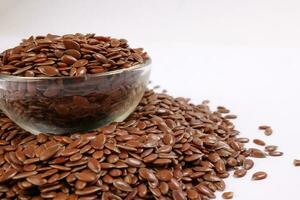 Flex seed flaxseed in small glass bowl over pile on white background closeup photo