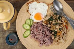 Thai fusion stair fried chicken with Thai basil and cashew nut with health brown rice fried egg sauce cucumber on woody plate over rustic wood background tin mug fork spoon photo