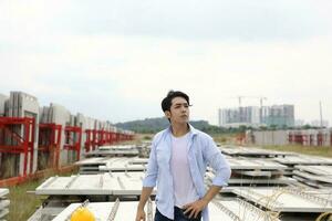 Asian man malay worker engineer management at construction site hard safety hat helmet hand on waist look forward photo