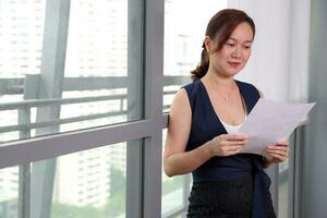 beautiful attractive middle age southeast asian woman home office work read see document standing near glass window urban daylight window background photo