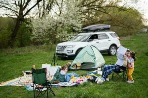 Mother hold europe map, with children sit on chair against car on picnic. photo