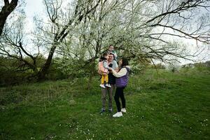 Family with two daughters in spring meadow on the background of a flowering tree. photo