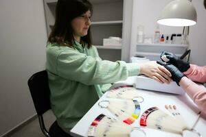 Manicure master working with female client in beauty salon. Manicurist makes woman nail. photo