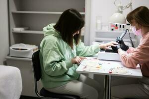 Manicure master working with female client in beauty salon. Woman chooses color of nail polish from palette. photo