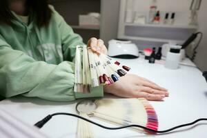 Manicure master working with female client in beauty salon. Woman chooses color of nail polish from palette. photo