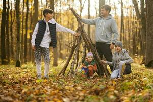 Children with father constructs a house from sticks in autumn forest. photo