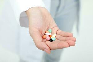 Asian doctor holding medicine capsule tablets pills on palm of hand photo