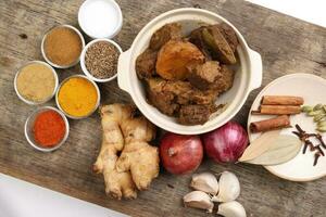 Beef bhuna dry curry with potato in ceramic bowl ingredients chilli cumin coriander turmeric powered salt onion garlic ginger bay leaf cinnamon cardamom clove over rustic wood background photo