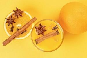 Fresh orange cinnamon star anise clove spice juice in glass on white yellow background photo