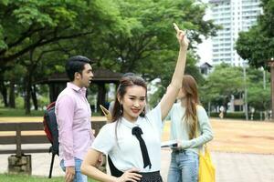 Young asian malay chinese man woman outdoor park walk stand study talk discuss point laptop file book backpack female look forward ok finger sign photo