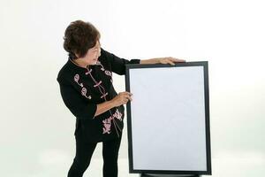 Elderly asian Chinese female wearing black tang samfu on white background pointing white black board copy text space photo