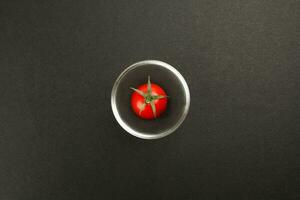 Red ripe cherry tomato with stem on black paper background copy text space mini glass bowl photo