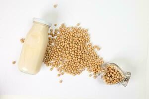 Soyabeans pouring from hart shape glass bottle around bottle of soya bean milk on white background photo