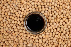 Soya sauce in small glass bowl on bed of soyabean background photo