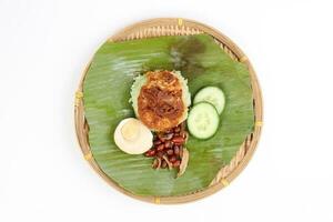 Nasi Lemak fragrant rice cooked in coconut milk served with sambal friend peanut anchovy boiled egg packed in banana leaf on round bamboo plate on white background photo