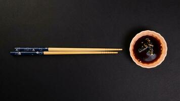 Bamboo wooden chopsticks and chili soya sauce in small ceramic bowl dish on black background photo