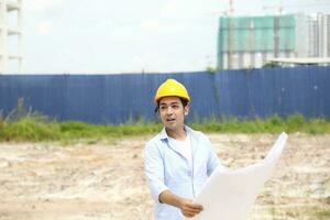 Asian man malay worker engineer management hard hat safety helmet at construction site reading seeing plan blueprint photo