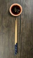 Bamboo wooden chopsticks and chili soya sauce in small ceramic bowl dish on rustic wood background photo