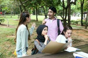 joven asiático malayo chino hombre mujer al aire libre parque libro archivo carpeta ordenador portátil computadora teléfono sentar estar estudiar mezclarse foto