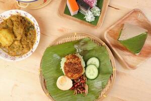 Nasi Lemak fragrant rice coconut milk with sambal friend peanut anchovy egg packed banana leaf round bamboo plate colorful nyonya kuih sweet desert palm leaf plate on wooden background photo