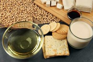 Soyabeans products soya beans flowing bamboo sieve wooden board on jute black stone slate background curd tofu oil milk sauce biscuit cookies photo