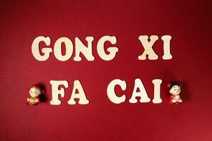 Wooden alphabet sign lettering Gong Xi Fa Cai Chinese New Year on maroon red paper background figurine photo