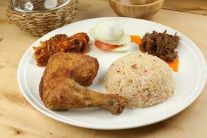 Indonesian royal dish nasi bojari with deep spiced deep fried chicken leg sambal prawn curry beef rendang boild egg cucumber and tomato slice photo