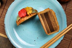 Colourful flower decorated mooncake Chinese mid autumn festival cut slice on blue ceramic plate background on bamboo food mat photo