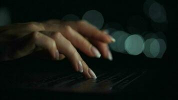 Accelerated video of female hands is typing on a laptop at night. Blurred lights on the background. Quick motion