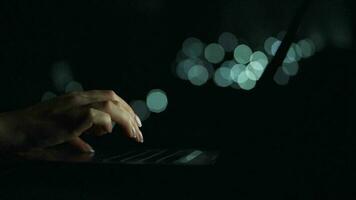 Accelerated video of female hands is typing on a laptop at night. Blurred lights on the background. Quick motion