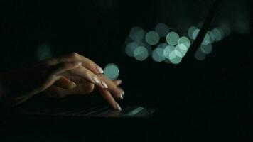 Accelerated video of female hands is typing on a laptop at night. Blurred lights on the background. Quick motion