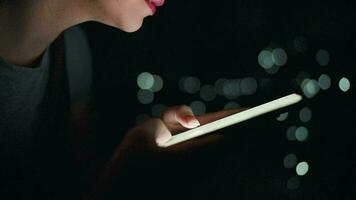 mujer es mecanografía en un teléfono inteligente a noche. borroso luces en el antecedentes video