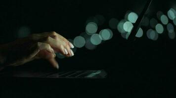 Accelerated video of female hands is typing on a laptop at night. Blurred lights on the background. Quick motion