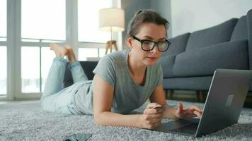 Frau mit Brille ist Lügen auf das Fußboden und Arbeiten auf ein Laptop. Konzept von Fernbedienung Arbeit video