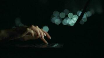 Accelerated video of female hands is typing on a laptop at night. Blurred lights on the background. Quick motion