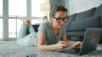 Woman with glasses is lying on the floor and working on a laptop. Concept of remote work video