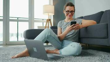 casualmente vestito donna seduta su tappeto con il computer portatile e smartphone e Lavorando nel accogliente camera. a distanza opera al di fuori il ufficio video