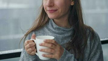caucasien femme séjours sur balcon pendant chute de neige avec tasse de chaud café ou thé. elle regards à le flocons de neige et respire video
