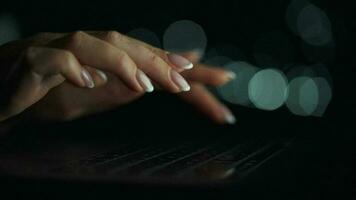 Accelerated video of female hands is typing on a laptop at night. Blurred lights on the background. Quick motion