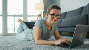 mujer con lentes es acostado en el piso y trabajando en un ordenador portátil. concepto de remoto trabajo video