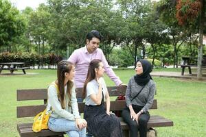 joven asiático malayo chino hombre mujer al aire libre parque libro archivo carpeta ordenador portátil computadora teléfono sentar estar estudiar mezclarse foto