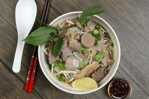 Vietnamese poh beef noodles soup broth with beef ball brisket tripe stomach parts been sprout thai basil lime in bowl on wooden table chopsticks spoon sauce photo