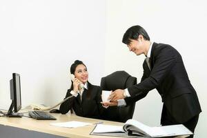 Young Asian male female wearing suit sitting at office desk serve give share coffee cup photo