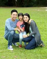 Southeast Asian family father mother daughter child posing on green grass happy outdoors photo