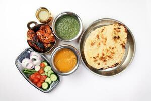 Spicy red Chicken grilled tikka tandoori nan bread green spinach curry yogurt sauce dal tomato cucumber onion salad set in metal stainless steel brass copper pot on white background photo