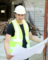 sur este asiático joven malayo hombre vistiendo blanco la seguridad casco amarillo chaleco mirando que lleva Plano plan al aire libre construcción sitio foto